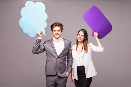 Beautiful young couple is holding speech bubbles, looking at camera and smiling, on gray backgroundの写真素材