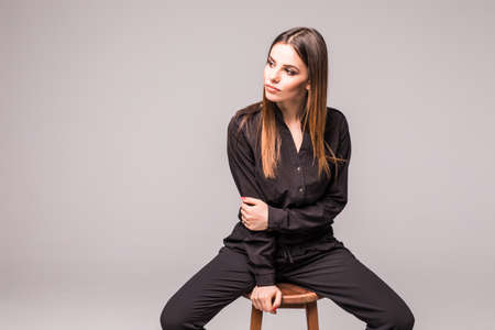 Portrait of a happy cheerful woman in black dress sitting on the chair and looking at camera over...