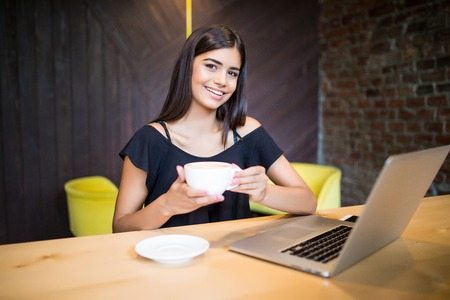 Beautiful brunette enjoying coffee and using laptopの写真素材