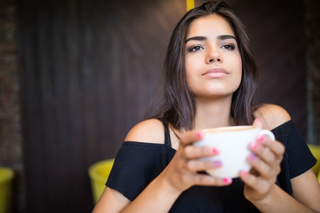 Portrait of young beautiful woman sitting in a cafe outdoor drinking coffeeの写真素材