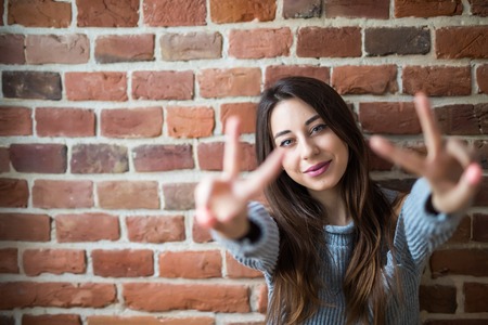 Beautiful young woman in casual wear smiling, standing against white brick wallの写真素材