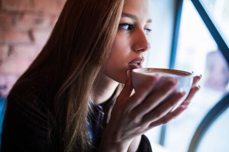 Close-up portrait of a pretty woman smiling and drinking coffee.の写真素材