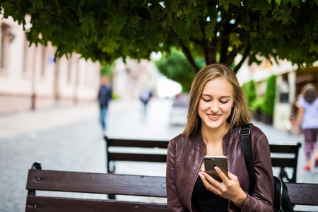 Attractive Young Adult Female Texting on Cell Phone Outdoors on a Bench.の写真素材
