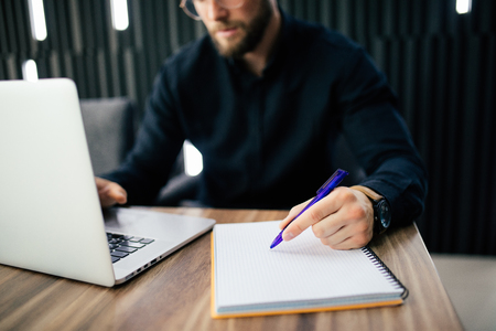Man is writing somethings on paper notebook and laptop computer on wooden table, business concept.の写真素材