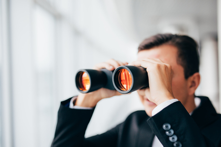 Handsome Business man looking with binoculars over panoramic windowsの写真素材