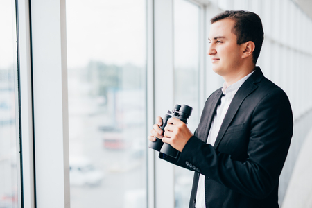 Business man looking with binoculars over panoramic windowsの写真素材