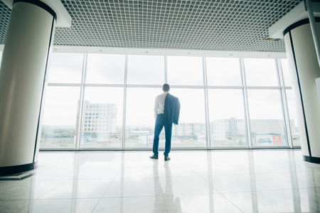 Young businessman with jacket over shoulders in modern office panoramic windowsの写真素材