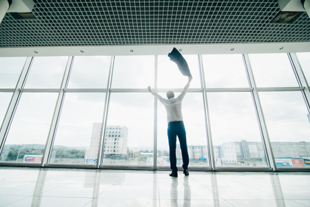 Well done job. Happy manager celebrate win or good deal with raised hands and up jacket over panoramic windowsの写真素材