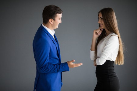 Smiling businesswoman and businessman are conversing against grey background.の写真素材