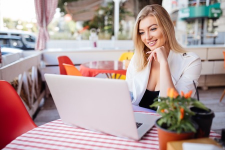 Beautiful young woman working on laptop and smiling while sitting outdoorsの写真素材