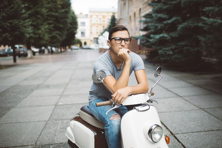 Handsome young man sitting on scooter on streetの写真素材
