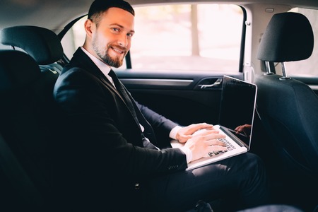 Handsome businessman working with laptop on the backseat of the carの写真素材