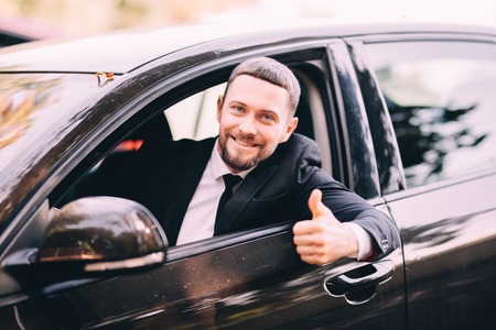Handsome beatded businessman in a car with thumbs upの写真素材