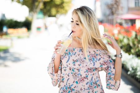 Beautiful girl with cold tankard outdoors. Smiling hipster girl with cup of drink on city street.の写真素材