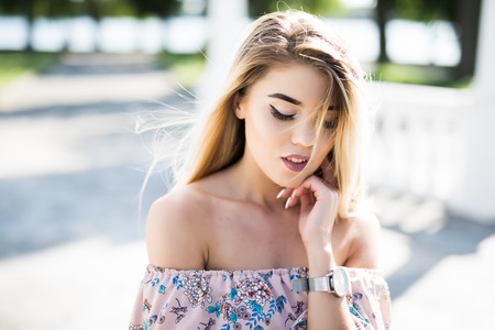 Close-up portrait of young blonde woman with blue eyes standing in the street. Beautiful girl in urban background wearing striped sweater. Female with straight hair.の写真素材