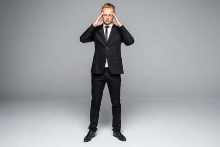 Handsome man in formal suit is touching his head having a headache, on gray backgroundの写真素材