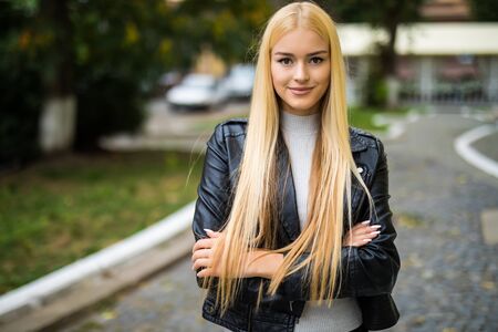 Attractive young girl is standing in street background outdoors, smiles, with crossed hands. She is wearing casual jeans outfitの写真素材