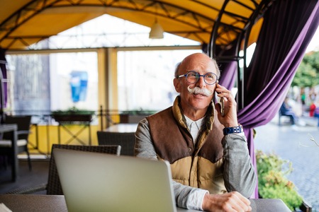 Senior businessman with smartphone and laptop in cafe