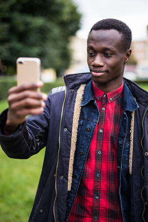 Photo of african man holding his cellphone in hands and make a selfie outdoors.の写真素材
