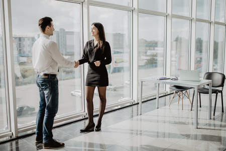 Businessman and businesswoman shaking hands together while standing in front of office building windowsの写真素材