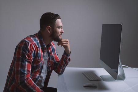 Businessman working at his desk with the blank screen of his desktop computer visible to the viewerの写真素材