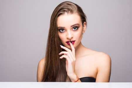 Pretty girl with big eyes and dark eyebrows, with naked shoulders, looking at camera and smiling, a model with light nude make-up, gray studio background, beauty photo, copy space, close up.の写真素材