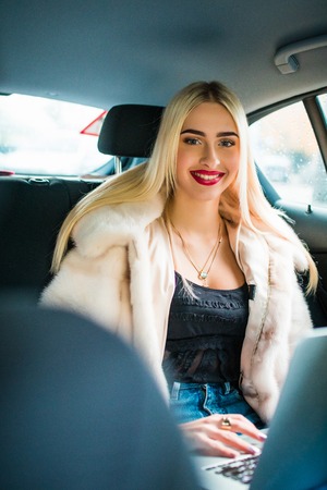 Photo of female entrepreneur talking on the phone while working with laptop in the car