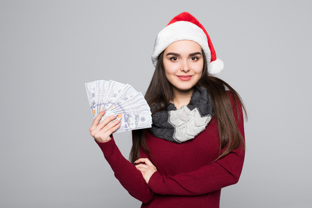 Happy young smiling woman in santa hat with dollar bills isolated on grayの写真素材