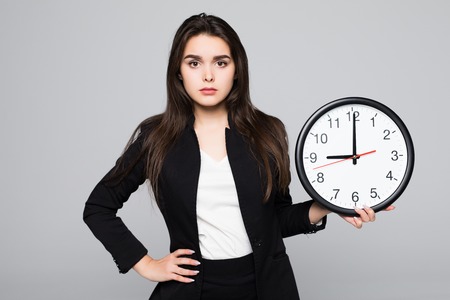 Business woman in suit which holding clock in hands and looking up. Isolated gray background
