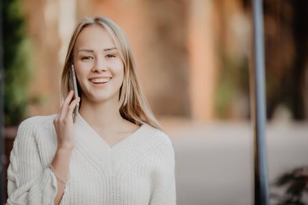 Closeup portrait of blonde girl speaking on phone on street.