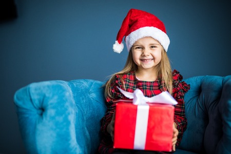 Beauty pretty girl wearing in dress and santa hat with Christmas gift sitting smiling at homeの写真素材