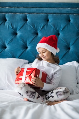 happy funny child girl with gifts in bed on Christmas morningの写真素材