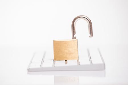 Open steel padlock lying on a white computer keyboard in a low angle view in a concpet of privacyの写真素材