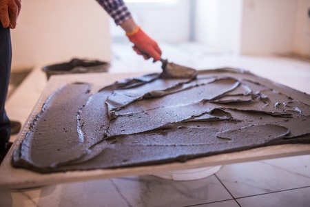 Laying Ceramic Tiles. Troweling mortar onto a concrete floor in preparation for laying floor tile.