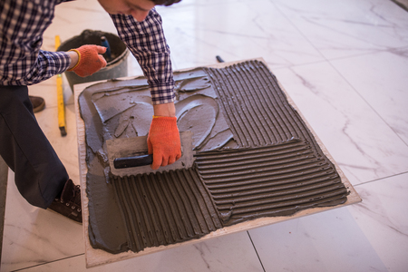 The workers hand is putting tiles adhesive to the wall with the notched trowel.