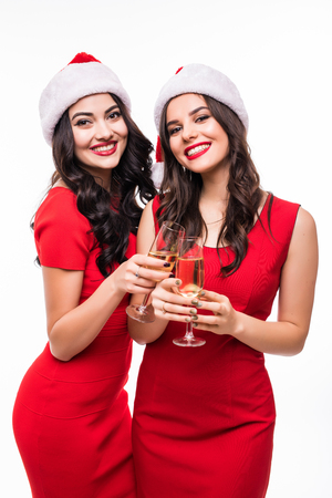 Portrait of two happy smiling girls in red dresses holding glasses with champagne while toasting and looking at camera isolated over whiteの写真素材