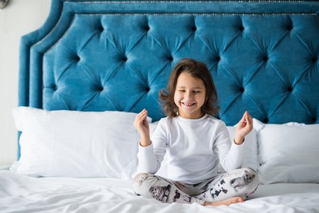 Photo of funny little girl trying to make lotus pose in bedの写真素材