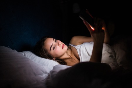A Woman using smartphone on bed at night