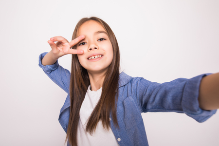 Portrait of funny little girl grimacing while taking a selfie isolated over white backgroundの写真素材