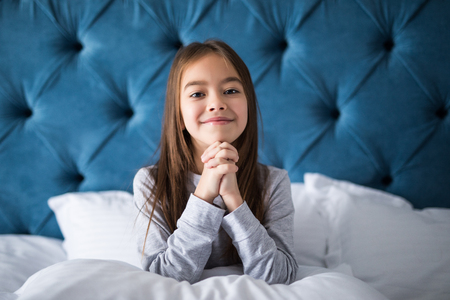 happy little girl with a pillow in bed at homeの写真素材