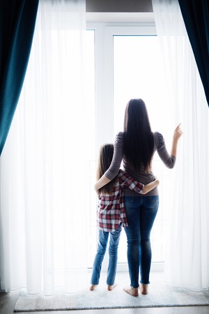 Young mother with daughter opening window curtains in cozy bedroom in the morning.の写真素材