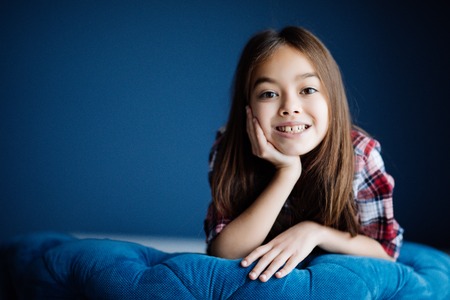 Little young kid sitting on chair with beauty smile look at camera at her roomの写真素材