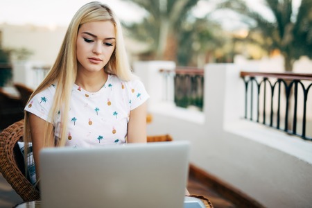 Modern girl is on the mobile phone while sitting in cafe on teracce. Young woman checking the information in the internet while having rest in a bar.の写真素材