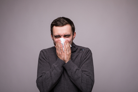 Closeup portrait of sick young man student or worker with allergy or germs cold, blowing his nose with kleenex, looking miserable unwell very sick, isolated on white background.の写真素材
