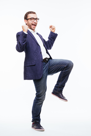 Excited elated happy young business man with beard in classic suit jumping and shouting over whiteの写真素材