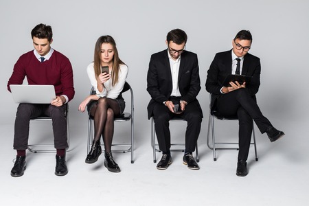 Stressful moment for people wait in queue. Nervous candidates for prestigious job wait with anxiety for interview, use modern smart phones and tablet, laptop for entartaining or self educationの写真素材