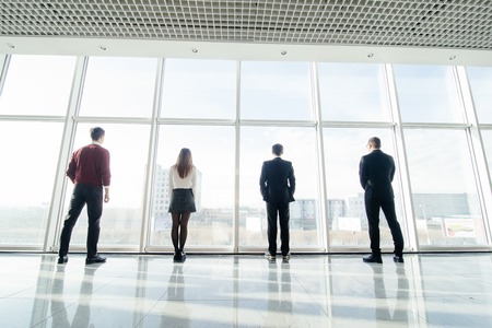 Back view silhouettes of four business partners looking thoughtfully out of a office window.の写真素材