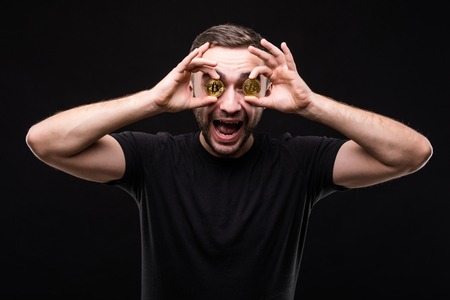 Young handsome man cover eyes with bitcoin coins isolated on blackの写真素材