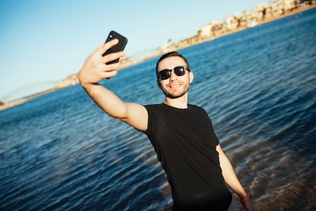 summer holidays and people concept - happy smiling young man in sunglasses and hat taking selfie on beachの写真素材