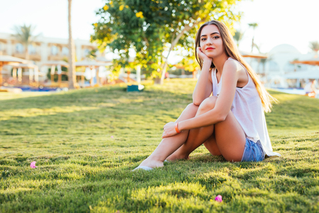 Beautiful woman sitting on the grass in the park on sunshineの写真素材